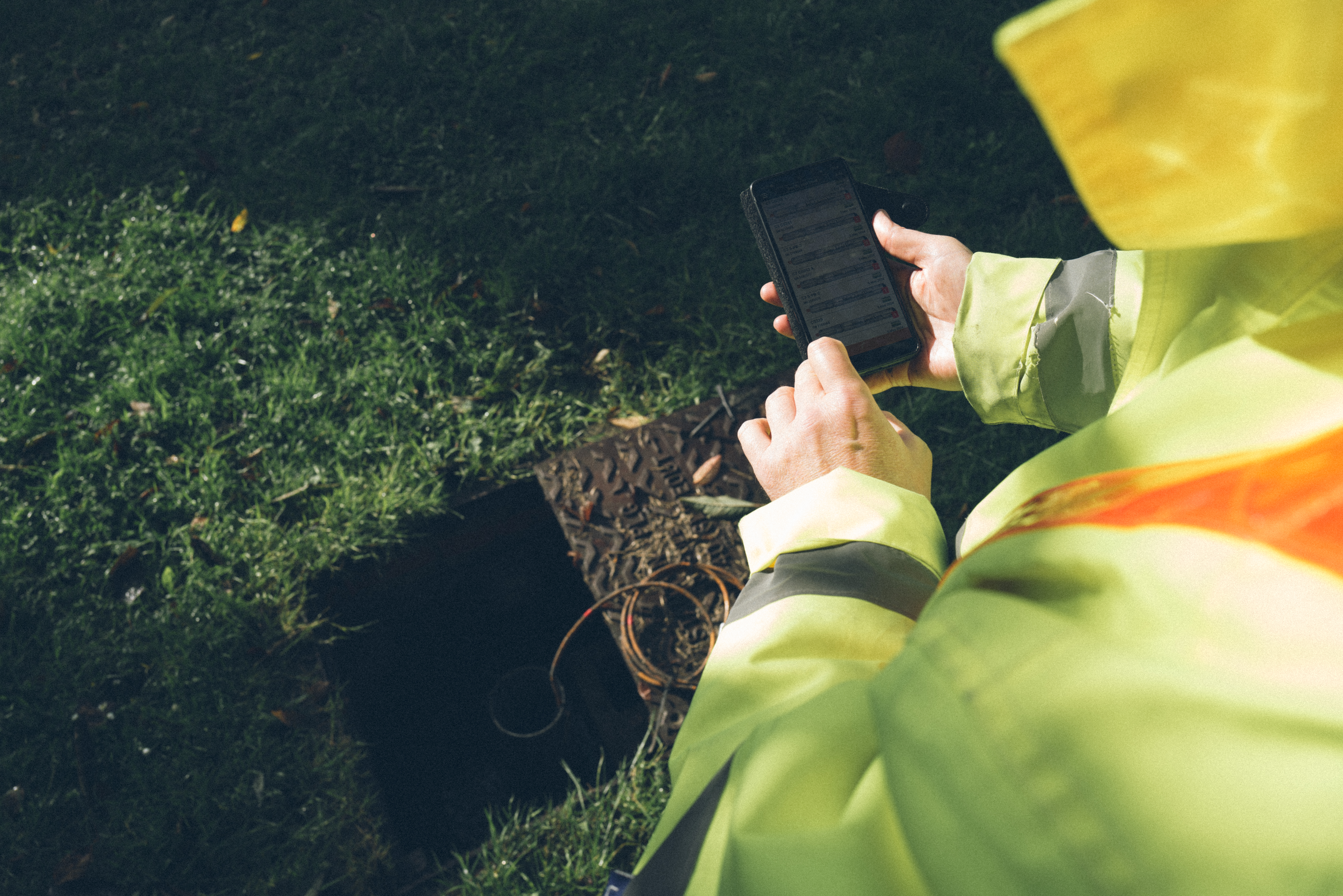 a person holding a mobile with a borehole in the background.