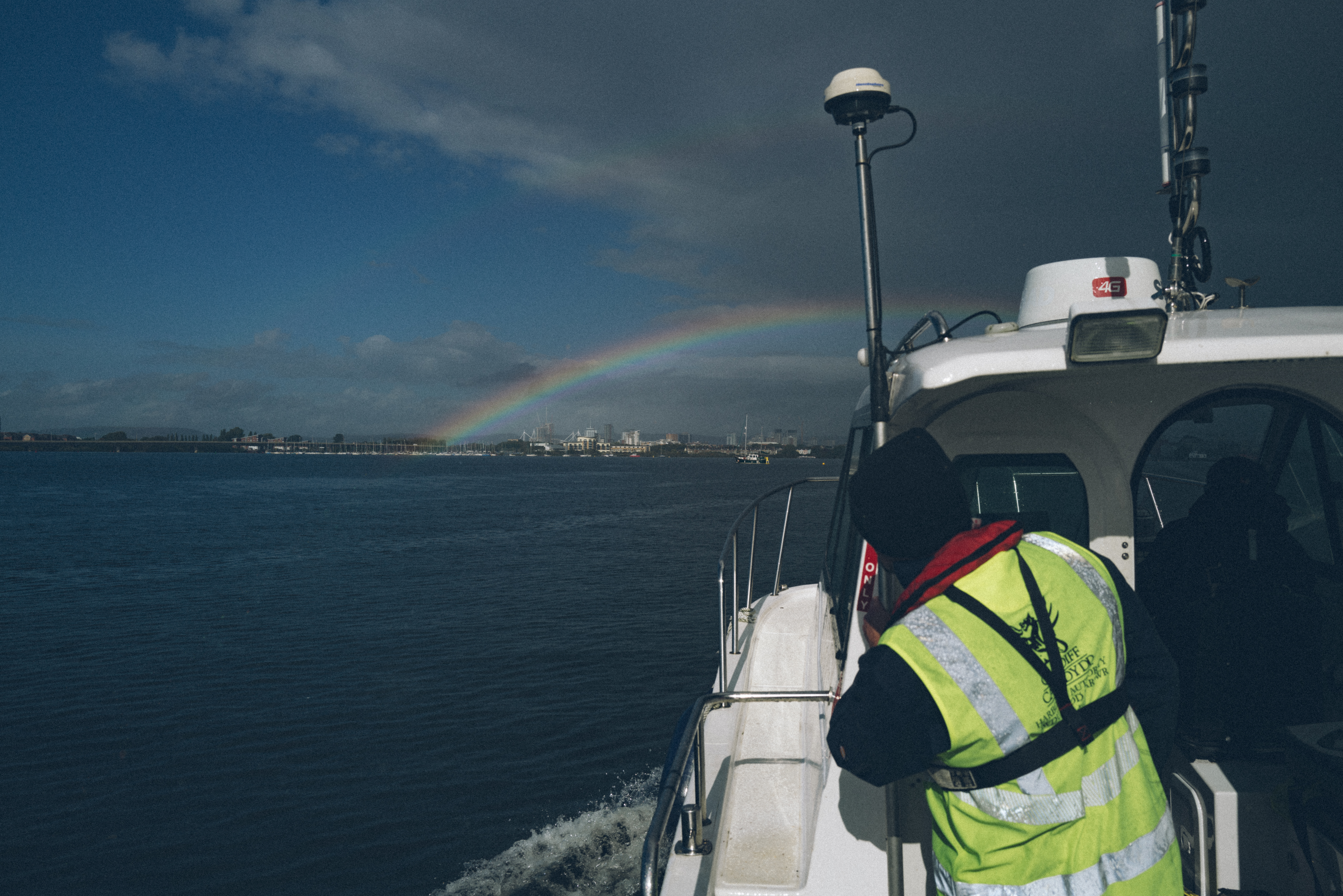 A person in hi-vis looking at a rainbow in the sky from the boat.