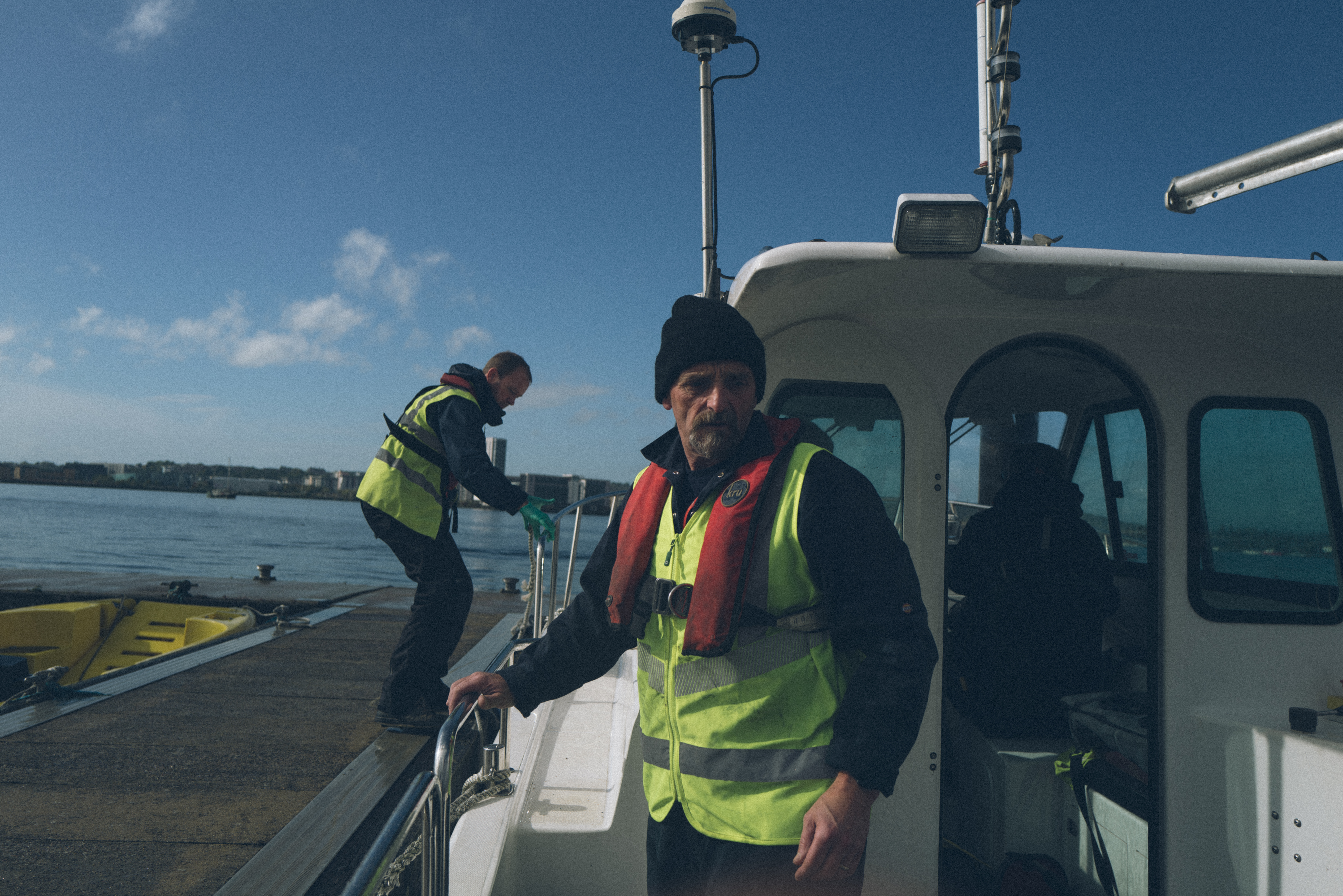 Two people in hi-vis one on the boat, one mooring the boat.